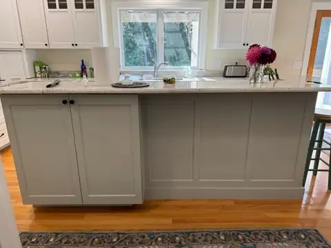Paneled island painted soft gray-green with a white stone top in front of white cabinets