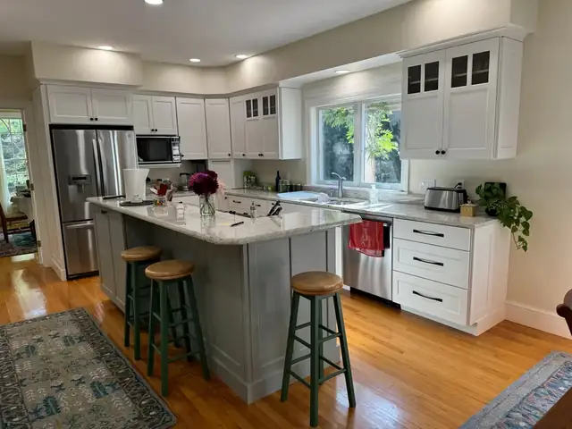 White kitchen with a sage gray island, stone countertop and green bar stools