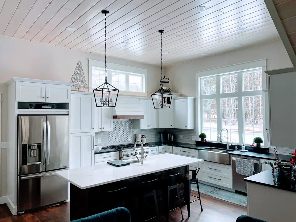 Custom kitchen cabinetry Gray ME: white cabinets, a dark island with a white top, lantern pendants and a wood plank ceiling by Laplante Cabinetry