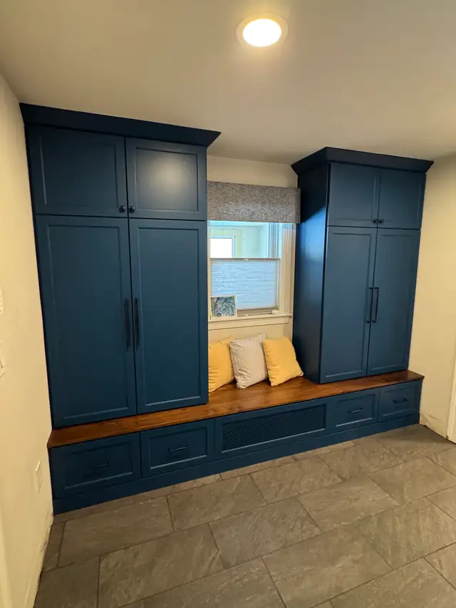 Custom built-in with tall navy cabinets on both sides of a window and a wood-topped bench seat with drawers