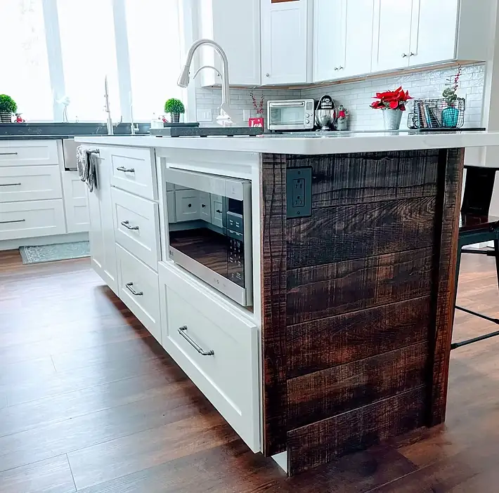 Custom white kitchen island with a dark reclaimed wood end panel and a built-in microwave drawer