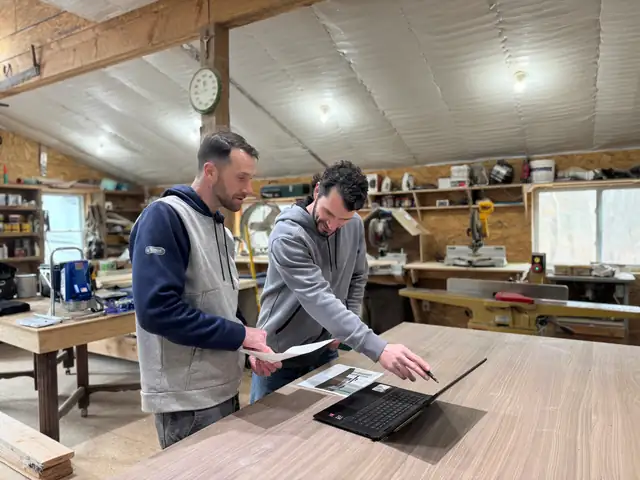Ryan and Kevin Laplante reviewing plans on a laptop at a workbench in their shop