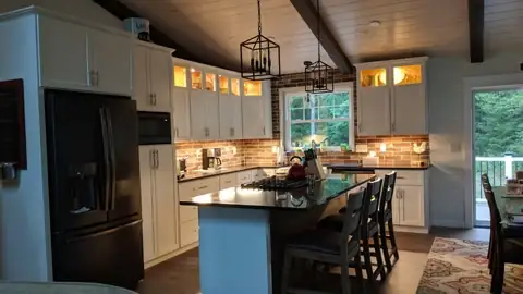 Kitchen with lit glass-front upper cabinets, a dark island, lantern pendants and a wood ceiling
