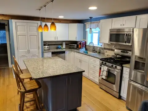 White kitchen with a dark painted island, granite top and amber glass pendants