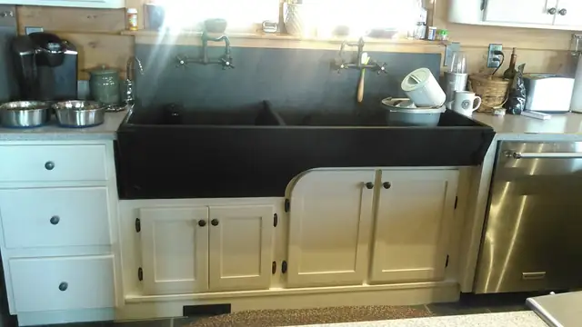 White custom sink base cabinets holding a wide black farmhouse sink with a bridge faucet