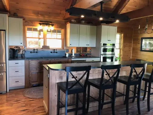 Kitchen by Laplante Cabinetry with white upper cabinets, a rustic wood island with black counters, X-back stools and a wood beam ceiling